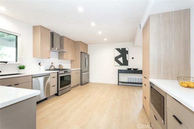 kitchen featuring stainless steel appliances, light countertops, wall chimney range hood, light wood finished floors, and modern cabinets