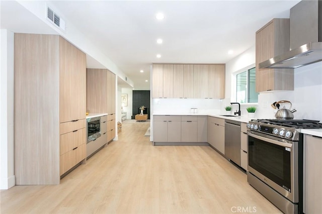 kitchen with visible vents, modern cabinets, stainless steel appliances, light brown cabinetry, and wall chimney range hood