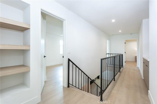 hallway with light wood finished floors, visible vents, baseboards, an upstairs landing, and recessed lighting