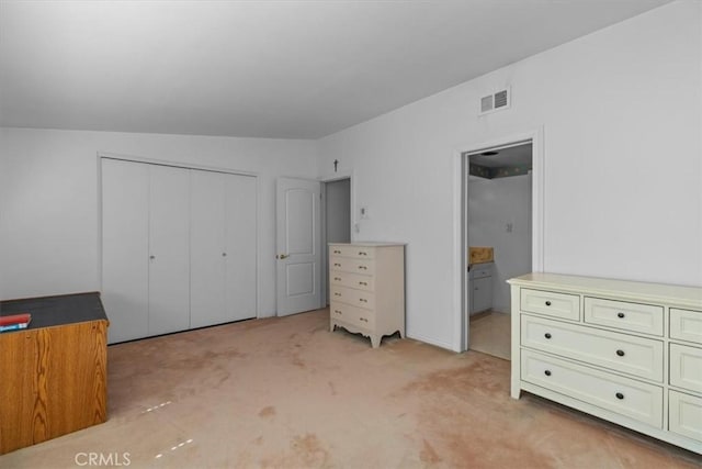 unfurnished bedroom featuring a closet, ensuite bath, visible vents, and light colored carpet