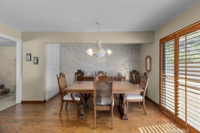 dining space featuring baseboards, an accent wall, stairway, an inviting chandelier, and light wood-style floors