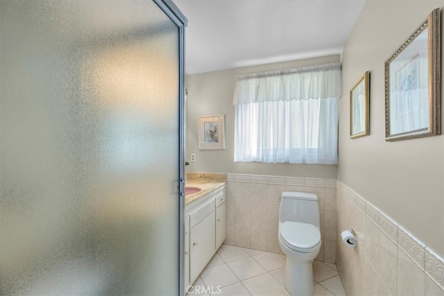 full bath featuring a stall shower, toilet, tile patterned flooring, vanity, and tile walls