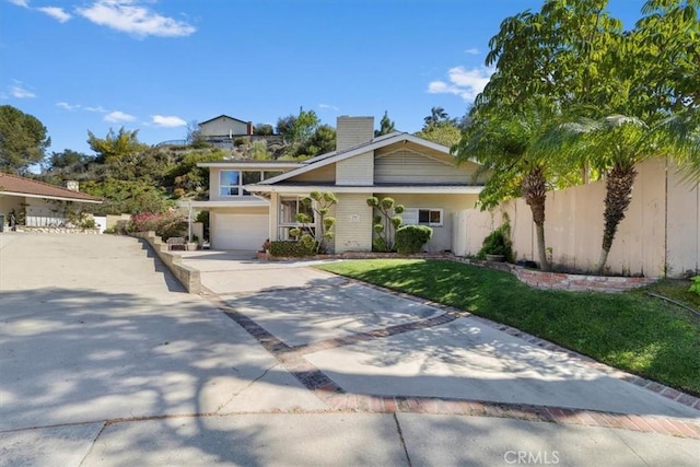 view of front of house with a chimney, an attached garage, a front yard, fence, and driveway