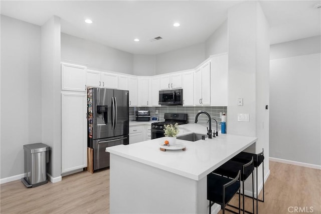 kitchen with a sink, tasteful backsplash, appliances with stainless steel finishes, a peninsula, and white cabinets