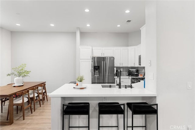 kitchen with a breakfast bar, stainless steel refrigerator with ice dispenser, a sink, white cabinetry, and a peninsula