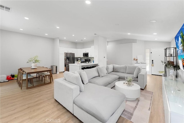 living room with visible vents, recessed lighting, light wood-style floors, and vaulted ceiling