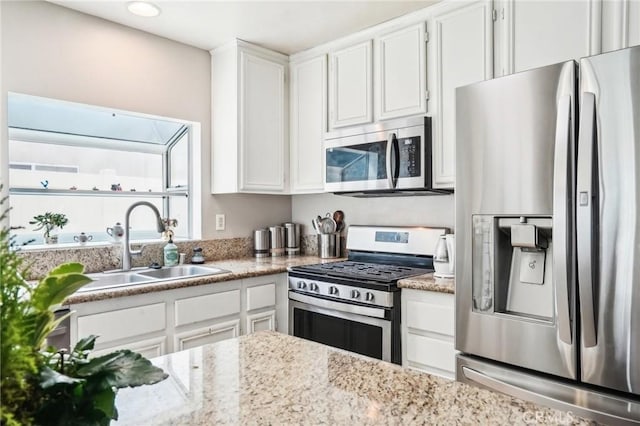 kitchen with white cabinetry, appliances with stainless steel finishes, light stone counters, and a sink