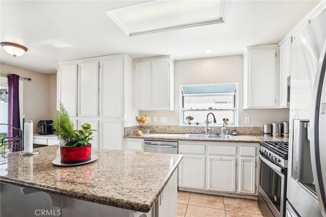 kitchen with light stone counters, light tile patterned flooring, a sink, white cabinets, and appliances with stainless steel finishes