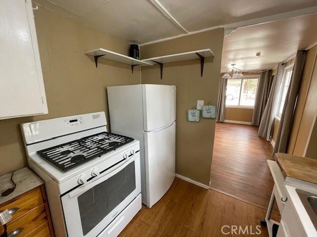 kitchen with open shelves, white appliances, wood finished floors, and light countertops