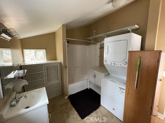 clothes washing area featuring a sink, laundry area, and stacked washer / dryer