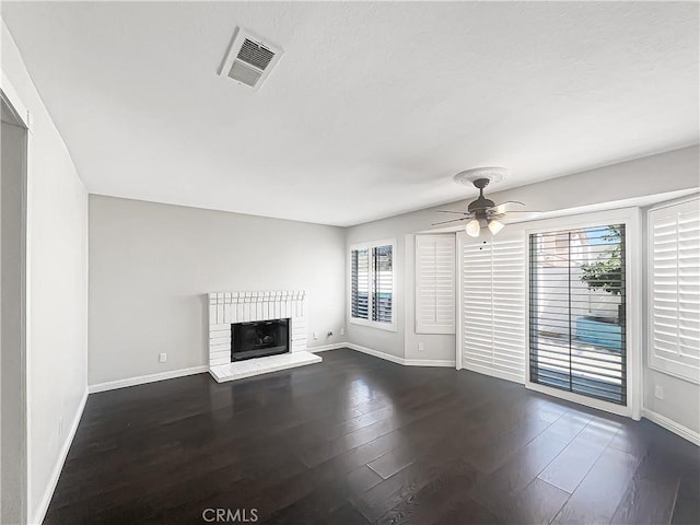 unfurnished living room with dark wood-style floors, visible vents, a ceiling fan, a brick fireplace, and baseboards