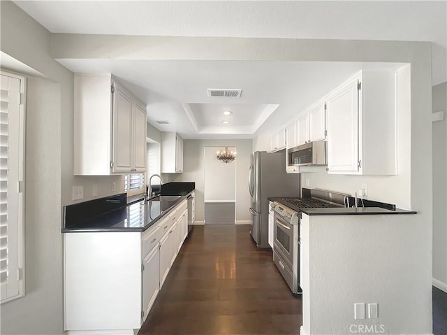 kitchen with stainless steel appliances, a sink, visible vents, dark countertops, and a raised ceiling