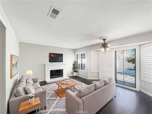 living room with visible vents, a ceiling fan, a glass covered fireplace, wood finished floors, and baseboards