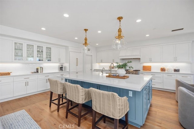 kitchen with white cabinetry, a kitchen breakfast bar, visible vents, and light wood-type flooring