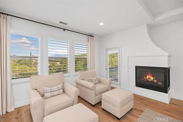 living area with visible vents, a glass covered fireplace, recessed lighting, light wood finished floors, and baseboards