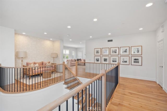 hall featuring wood finished floors, baseboards, visible vents, recessed lighting, and an upstairs landing