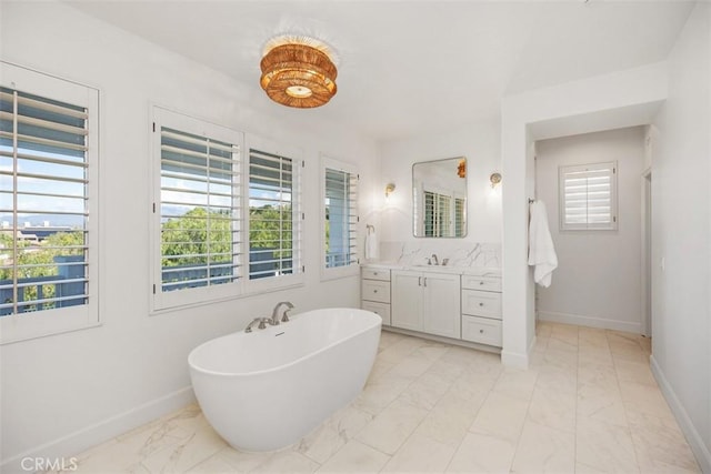 bathroom featuring marble finish floor, a freestanding bath, vanity, and baseboards