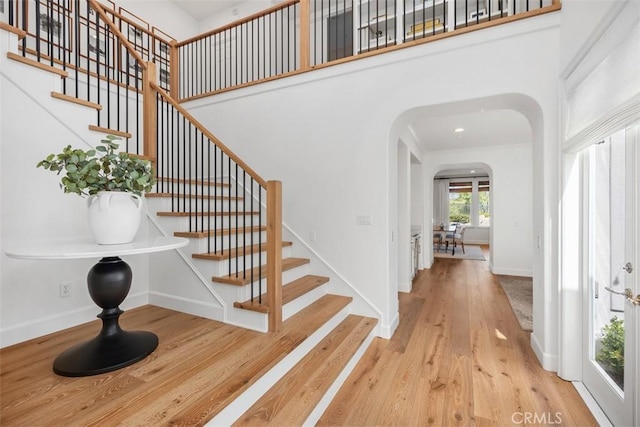 entrance foyer featuring arched walkways, baseboards, a towering ceiling, and wood finished floors