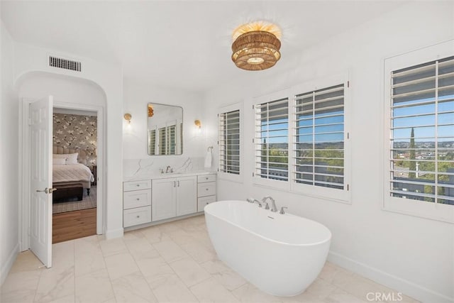 ensuite bathroom featuring visible vents, baseboards, a soaking tub, marble finish floor, and vanity