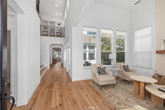 corridor featuring plenty of natural light, wood finished floors, arched walkways, and a towering ceiling