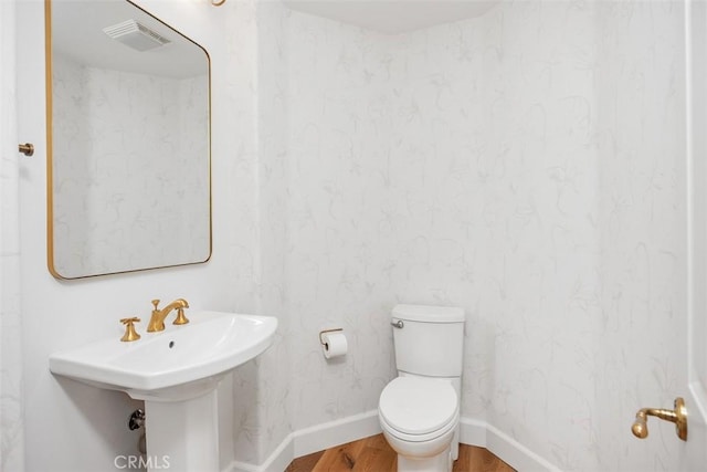 half bath featuring visible vents, toilet, a sink, wood finished floors, and baseboards