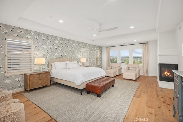 bedroom featuring light wood-style flooring, a tray ceiling, recessed lighting, wallpapered walls, and baseboards