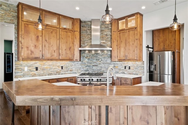 kitchen with a barn door, stainless steel appliances, decorative backsplash, wall chimney exhaust hood, and glass insert cabinets