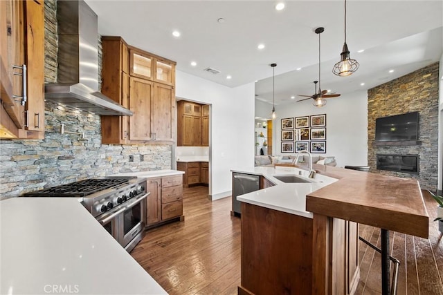 kitchen featuring stainless steel appliances, open floor plan, a sink, wall chimney exhaust hood, and hardwood / wood-style flooring