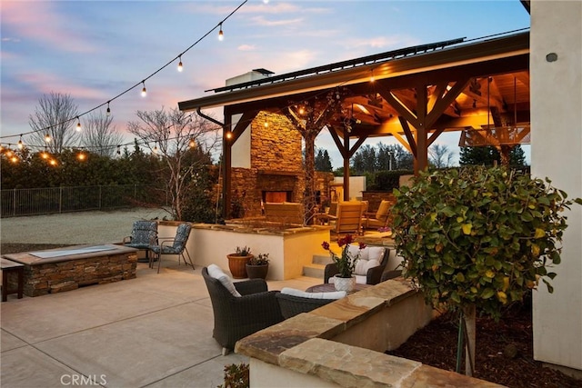 patio terrace at dusk featuring an outdoor living space with a fireplace, fence, and a gazebo