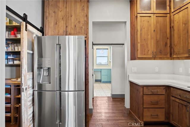 kitchen featuring a barn door, brown cabinetry, stainless steel fridge with ice dispenser, dark wood-style flooring, and light countertops