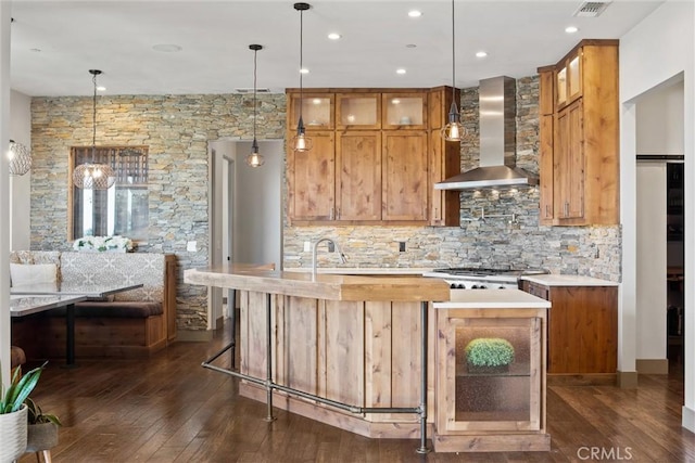 kitchen with dark wood-style floors, light countertops, stainless steel gas stovetop, glass insert cabinets, and wall chimney exhaust hood