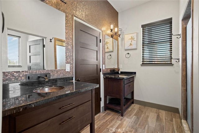 bathroom featuring baseboards, two vanities, a sink, and wood finished floors