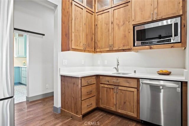 kitchen with a barn door, stainless steel appliances, a sink, light countertops, and dark wood-style floors