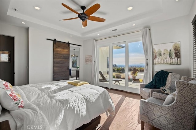 bedroom featuring a barn door, recessed lighting, wood finished floors, access to exterior, and a raised ceiling