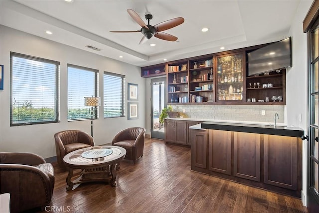 bar featuring visible vents, decorative backsplash, a raised ceiling, dark wood finished floors, and wet bar