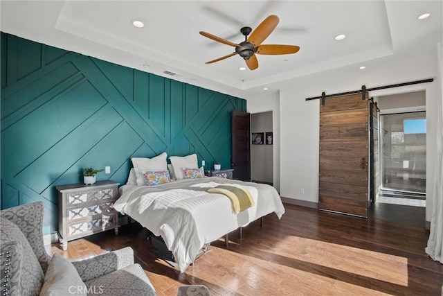 bedroom featuring a tray ceiling, visible vents, a barn door, an accent wall, and wood finished floors