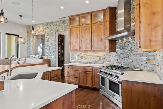 kitchen featuring a sink, light countertops, double oven range, brown cabinets, and wall chimney exhaust hood