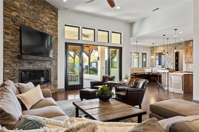 living area featuring a ceiling fan, visible vents, wood finished floors, and a stone fireplace