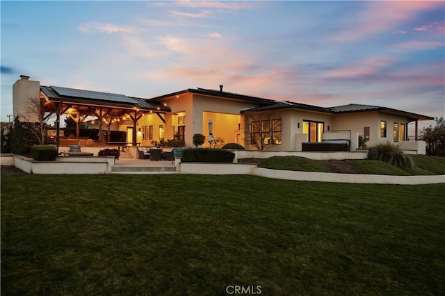 back of house featuring a lawn, solar panels, a patio, an outdoor living space, and stucco siding