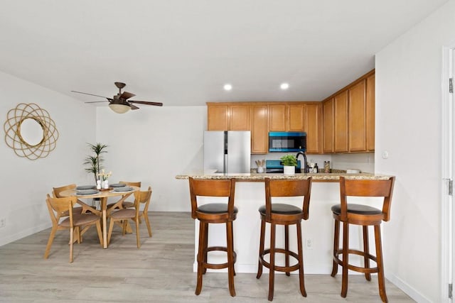 kitchen featuring black microwave, a peninsula, stove, freestanding refrigerator, and light wood finished floors