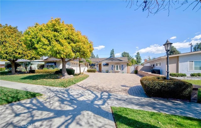 ranch-style house with decorative driveway, fence, a front lawn, and an attached garage