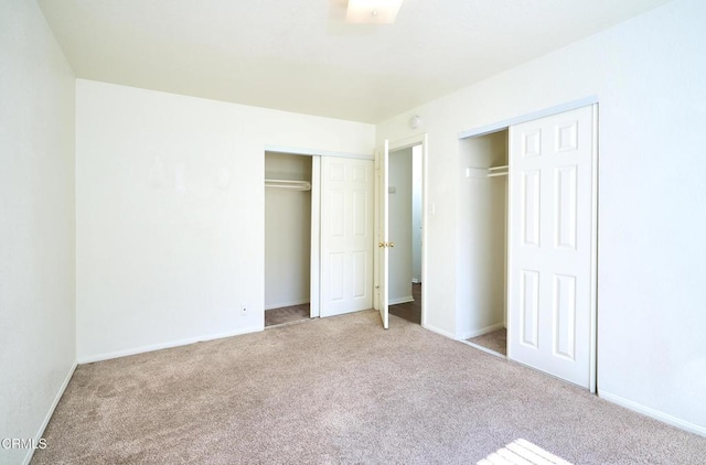 unfurnished bedroom with carpet floors, baseboards, and two closets