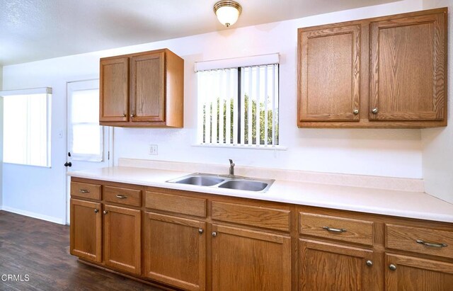 kitchen featuring dark wood-style flooring, light countertops, brown cabinetry, a sink, and baseboards