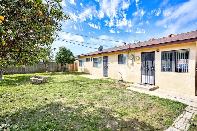 rear view of house with an outdoor fire pit, fence, and stucco siding