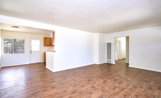 unfurnished living room with dark wood-style floors, visible vents, a textured ceiling, and baseboards