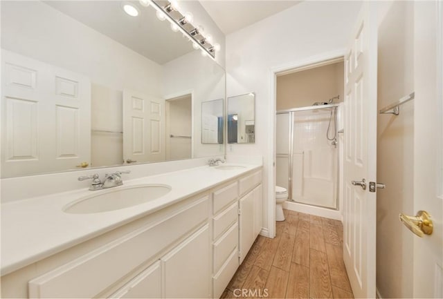 bathroom featuring toilet, a stall shower, a sink, and wood finished floors