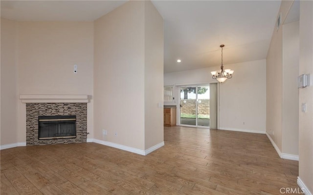 unfurnished living room featuring a chandelier, a fireplace, baseboards, and wood finished floors