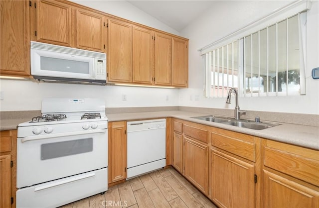 kitchen featuring light wood finished floors, lofted ceiling, light countertops, a sink, and white appliances