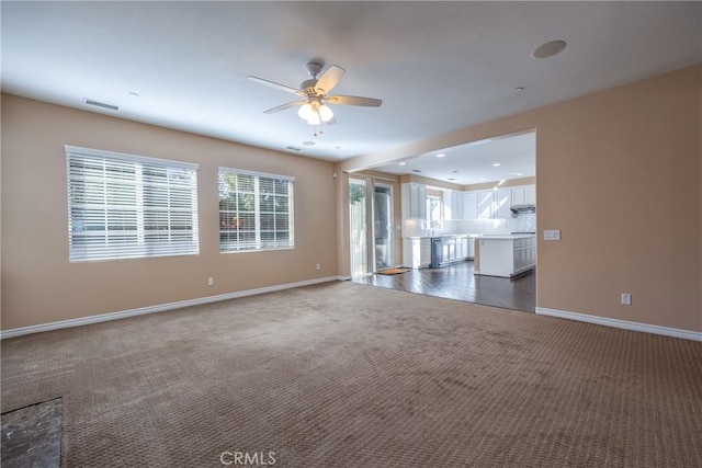 unfurnished living room with baseboards, visible vents, dark colored carpet, and a ceiling fan