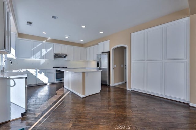 kitchen featuring arched walkways, light countertops, visible vents, stainless steel fridge, and exhaust hood